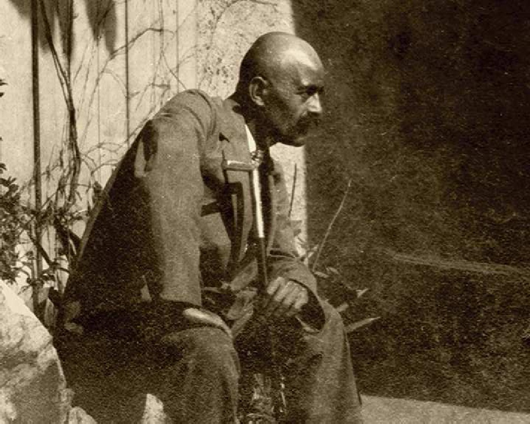 George Ivanovich Gurdjieff, seated, side profile, holding cane.