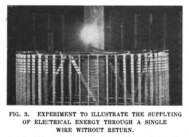 FIG. 3. Experiment to Illustrate the Supplying of Electrical Energy Through a Single Wire Without Return. An ordinary incandescent lamp, connected with one or both of its terminals to the wire forming the upper free end of the coil shown in the photograph, is lighted by electrical vibrations conveyed to it through the coil from an electrical oscillator, which is worked only to one fifth of one per cent. of its fully capacity.
